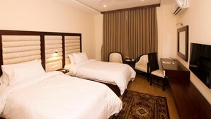 Quarto de hotel com duas camas, uma escrivaninha, uma cadeira, uma televisão e um ventilador de teto.