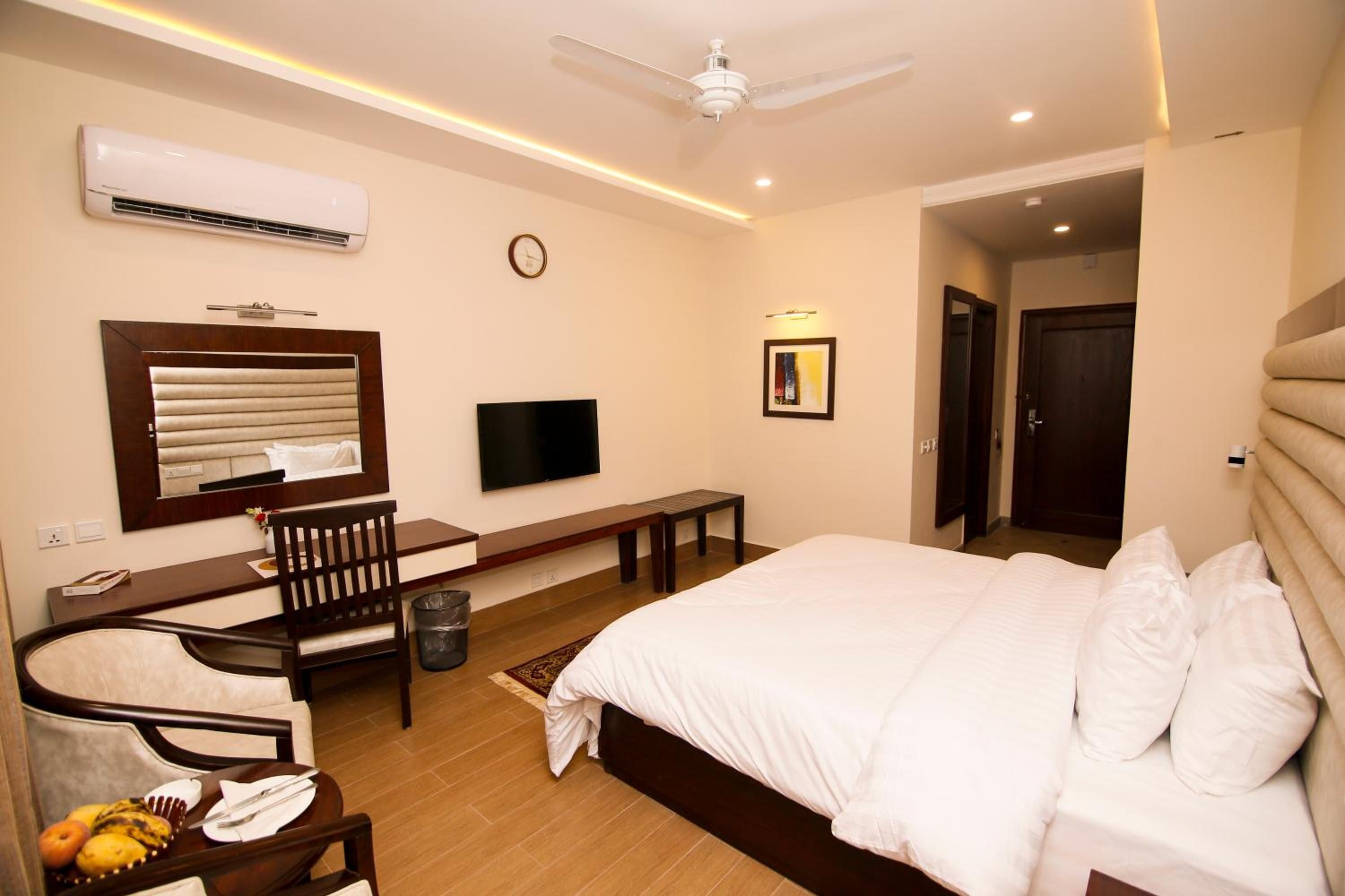 A hotel room with a bed, a desk with a chair, a television, and a clock on the wall.