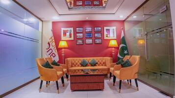 A lobby with a red wall, a sofa, two armchairs, a coffee table, and two flags.