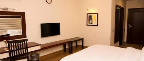 Una habitación de hotel con cama, escritorio, silla, televisión, reloj y puerta.