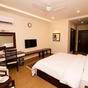 A hotel room with a bed, a desk, a chair, a television, a clock, and a door.