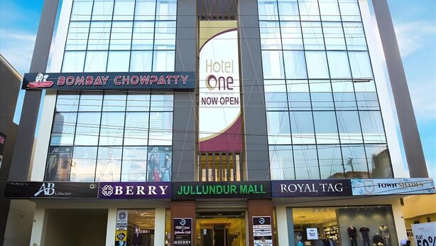 Hotel One, um hotel com fachada moderna, situado numa área comercial com lojas como Berry e Royal Tag.