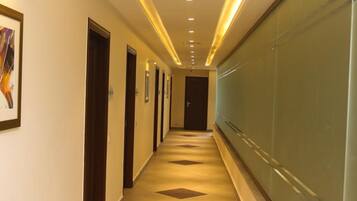 A long, narrow hallway with doors on one side and a glass wall on the other, featuring recessed lighting and patterned floor tiles.