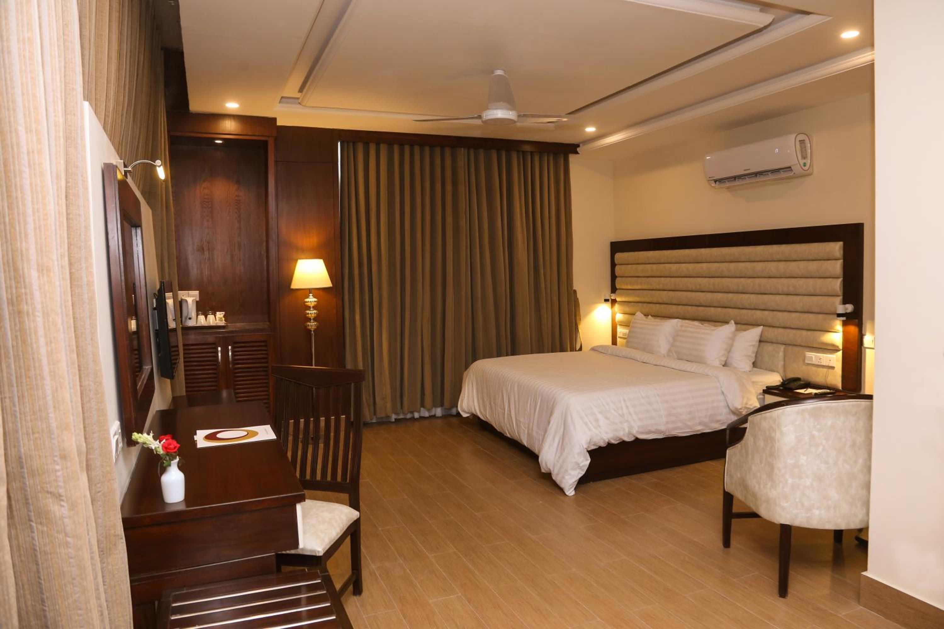 A hotel room with a bed, bedside table, lamp, and a desk with a chair.