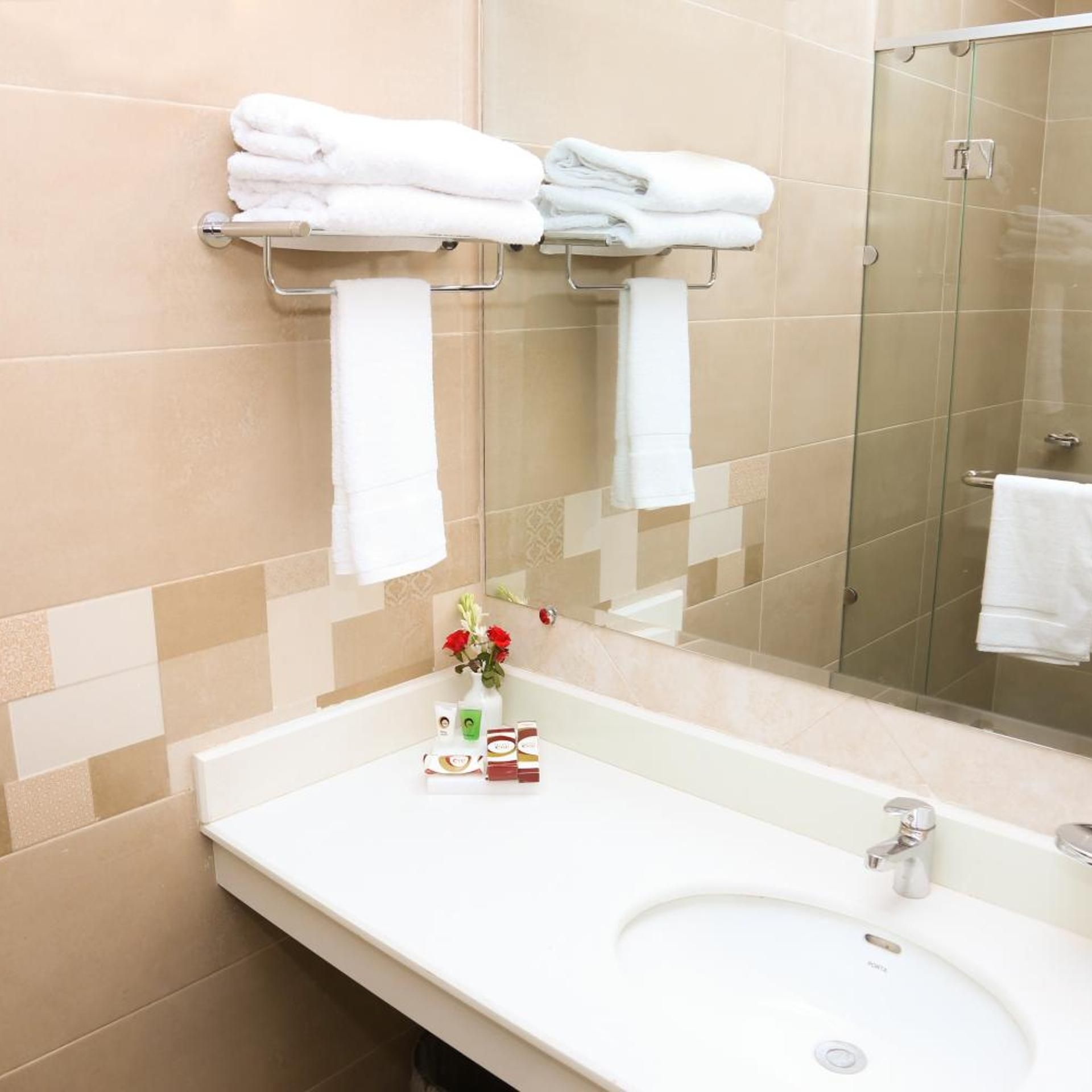 A bathroom with a white sink, a glass shower enclosure, and a towel rack with folded towels.