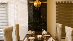 Mesa de jantar posta com cadeiras, parede decorativa e janela com persianas.