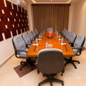 A conference room with a long wooden table, grey upholstered chairs, water bottles, and a floral centerpiece.
