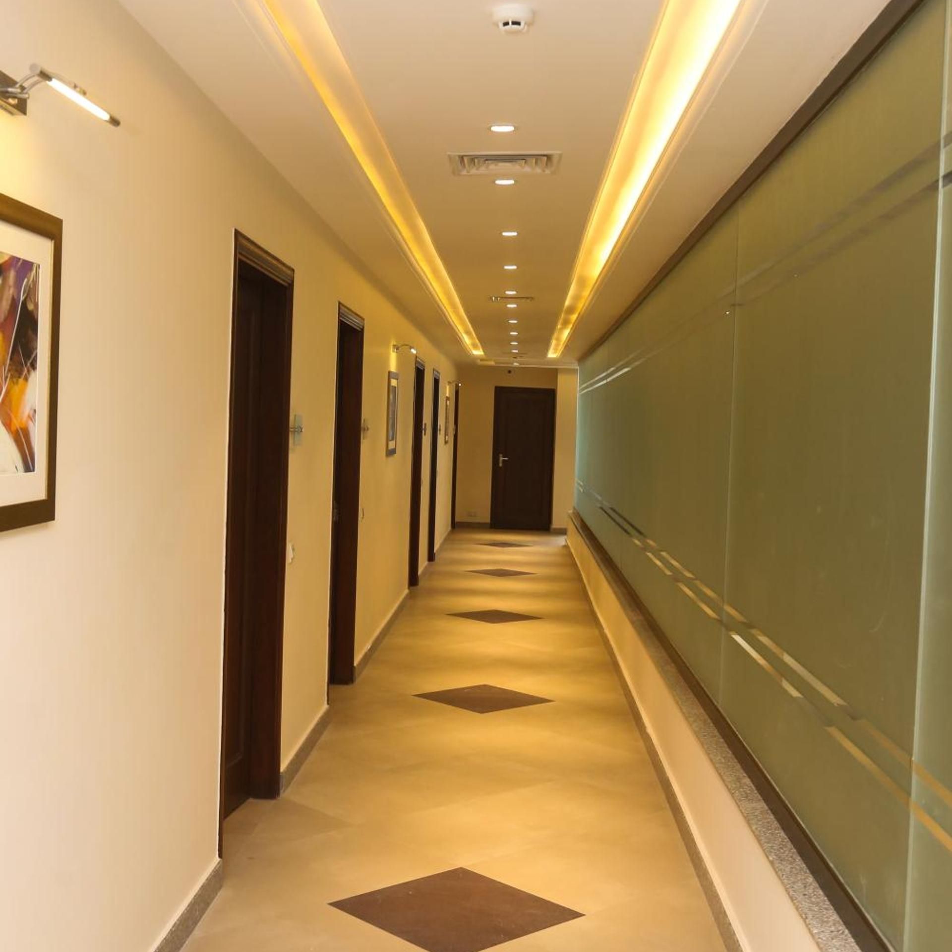 Corredor de hotel com um longo hall, portas e um muro de vidro de um lado.