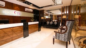 Uma área de recepção de hotel com balcão, sofá e cadeiras estampadas.