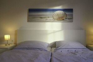 Ein Hotelzimmer mit einem Bett, zwei Nachttischlampen und einem gerahmten Bild von einer Muschel an der Wand.
