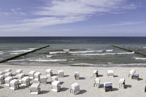 A beach with rows of white beach chairs and umbrellas, a wooden jetty, and calm ocean waves. - Holiday apartment, sound of the sea (Ostseebad Nienhagen)