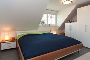 Ein Schlafzimmer mit Bett, Nachttisch, Kleiderschrank und Fenster.