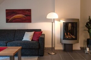 Ein modernes Wohnzimmer mit grauem Sofa, einer Stehlampe, einem Kamin und einem Bild an der Wand.