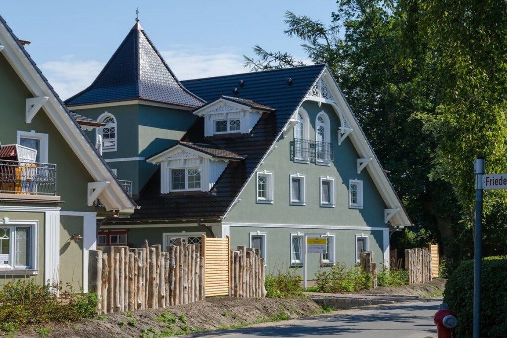 A multi-story building with a steeply pitched roof, a balcony with a railing, and a wooden fence in front.