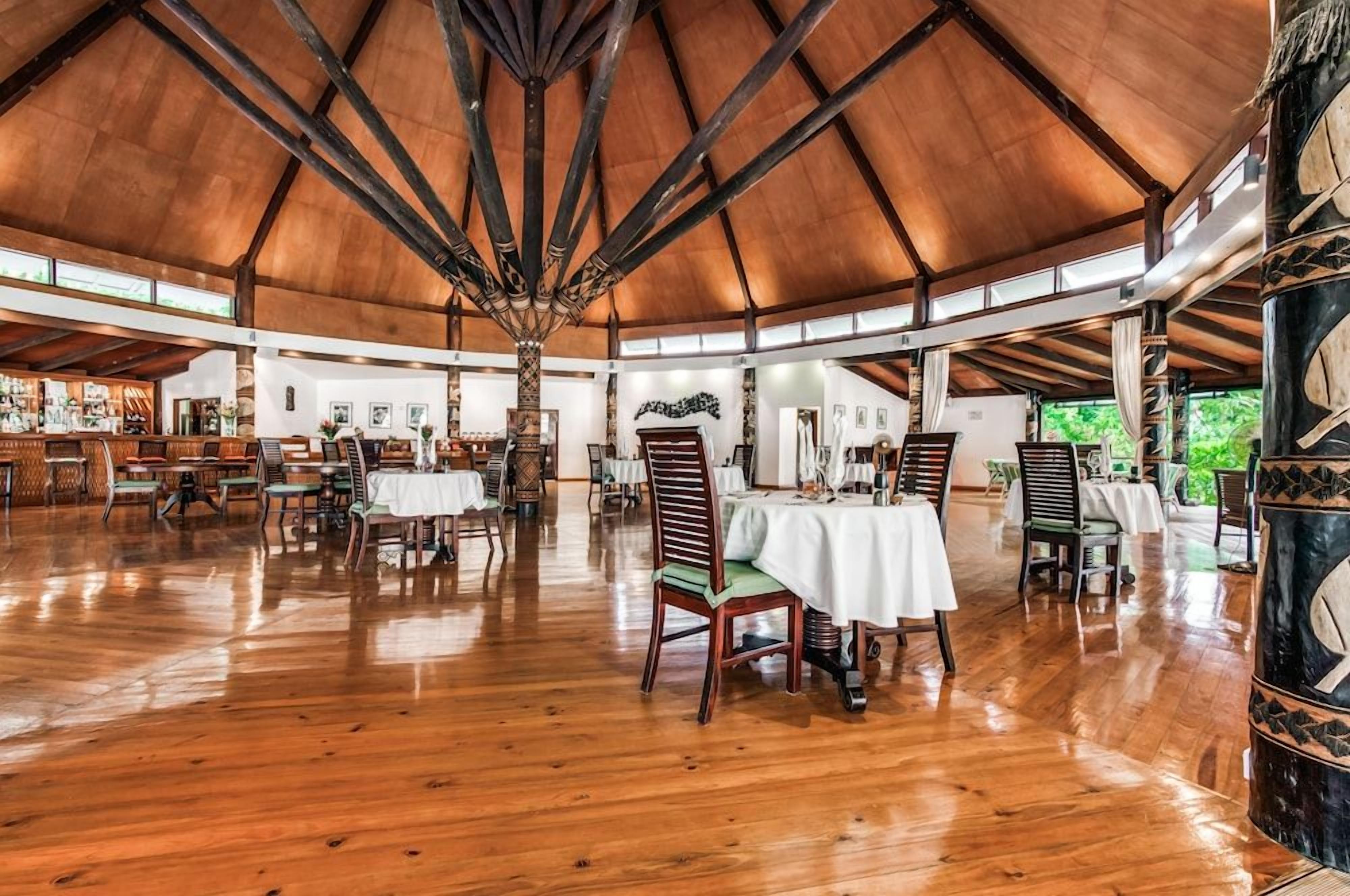 A spacious indoor area with high ceilings and wooden flooring, featuring multiple dining tables and chairs.