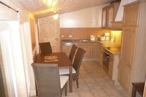 A compact kitchen with wooden cabinets, a dining table with chairs, and basic appliances. - "TUSCANY" with balcony and 2 bedrooms (Waren)