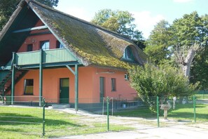 A traditional building with a steeply pitched roof, a green porch, and a fenced yard. - Holiday home with 1 bedroom (Alt-Schwerin)