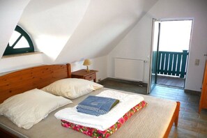 A bedroom with a sloped ceiling, a bed with a floral mattress cover, a nightstand with a lamp, and a view of a balcony through an open door. - Holiday home with 1 bedroom (Alt-Schwerin)