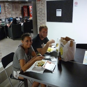 Two people seated at a table with food containers, a bottle, and a paper bag.