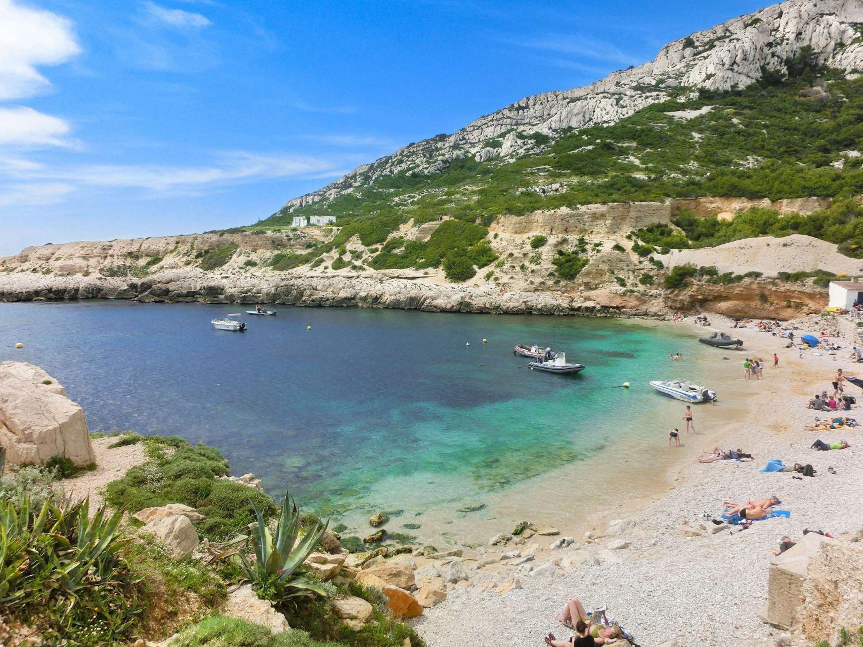 Une plage côtière avec des bateaux, des gens et un paysage rocheux.
