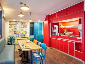 A dining area with a long table, blue chairs, and a red counter with a coffee machine. - Hotel F1 Marseille Provence (Les Pennes-Mirabeau)