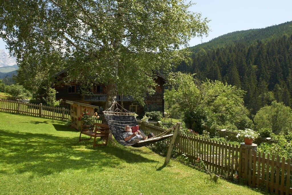 Une cabane en bois dotée d’un hamac et d’une terrasse en bois, entourée d’une clôture en bois et d’une végétation luxuriante.