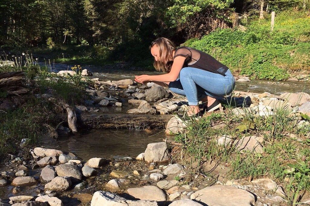 A person crouching near a rocky stream in a natural setting.
