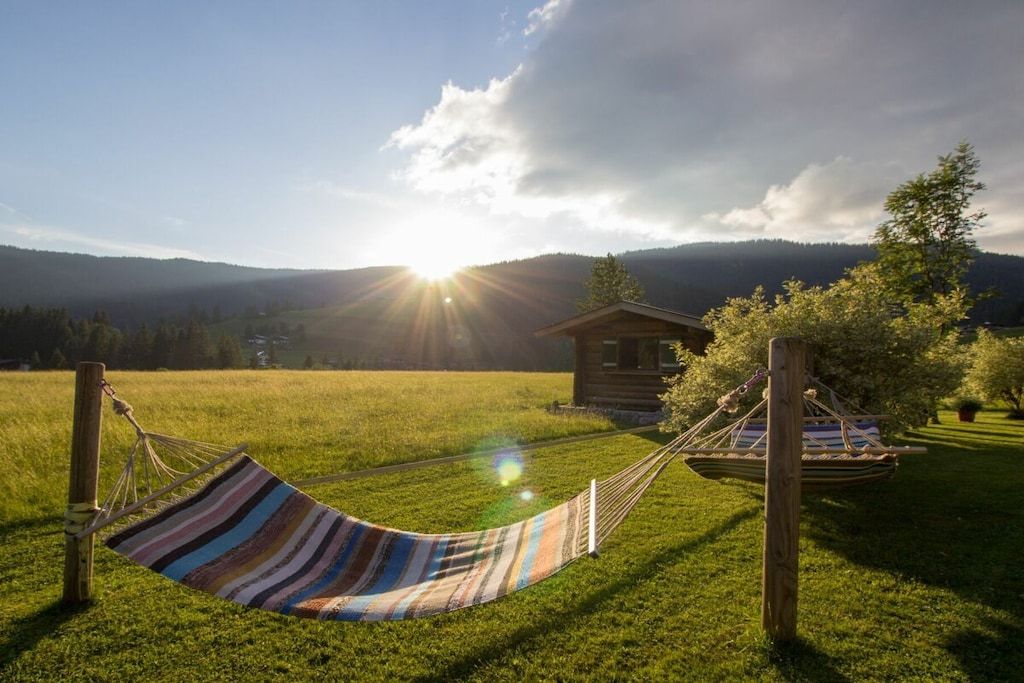 Un hamac dans un champ d’herbe, avec une cabane en bois en arrière-plan.