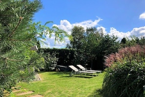 Ein Garten mit Rasenfläche, zwei Liegestühlen und einer überdachten Grillgegend.
