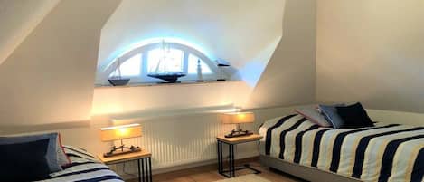 Quarto com duas camas, uma janela decorada com um navio e um radiador.