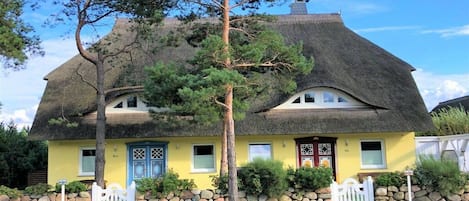 Een klassiek huis met rieten dak, een geel gevelpand, een stenen muur en een wit hekwerk.