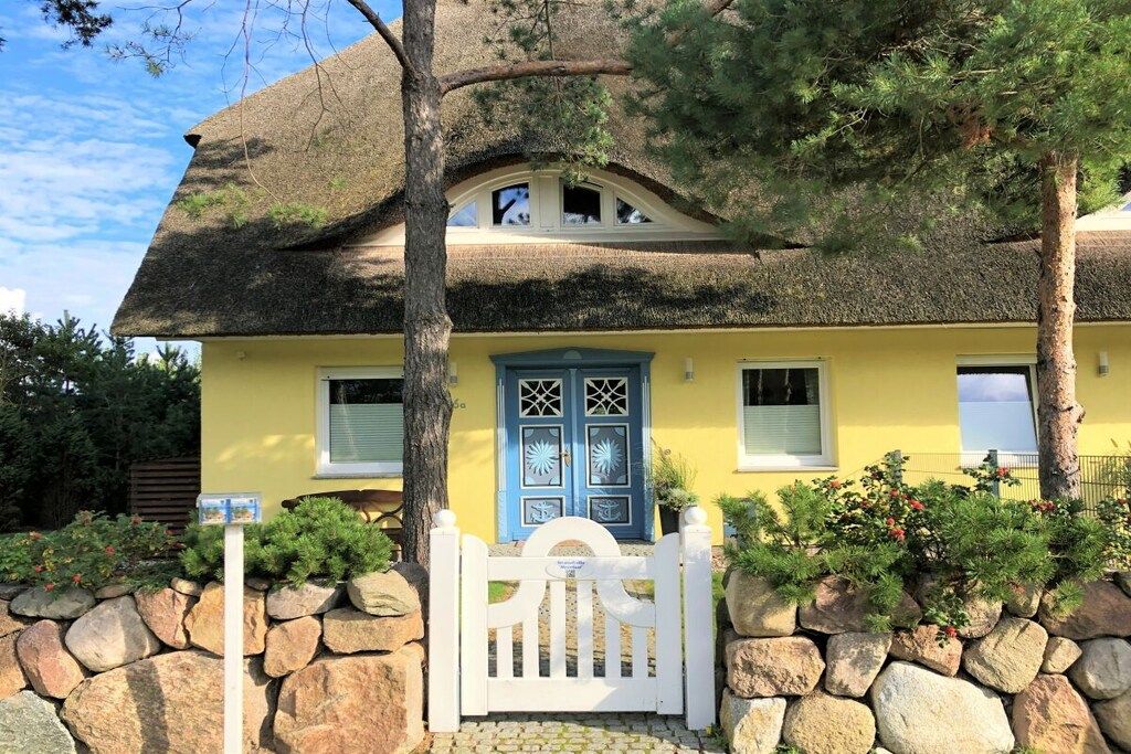 A yellow house with a thatched roof, a blue door, and a white gate.