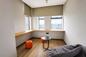 A corner room with a city view, a wooden floor, a small table, two orange stools, and a grey bean bag. - Slow Walker Youth Hostel (Chengdu)