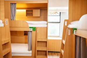 Habitación compacta y bien organizada con literas, un mueble pequeño y una ventana que deja entrar luz natural.