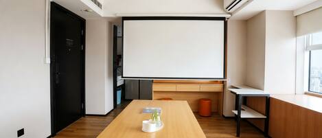 A modern meeting room with a large projection screen, wooden flooring, and a minimalist design.