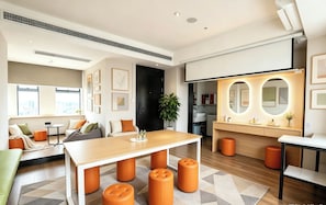 A modern hotel room with a wooden dining table, orange ottomans, a sofa, and a large mirror with circular lights. - Slow Walker Youth Hostel (Chengdu)