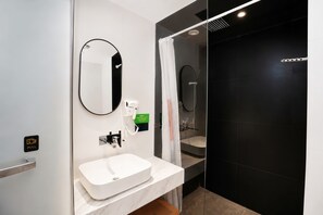 A modern bathroom with a white sink, a mirror, a shower with a glass door, and a black wall. - Slow Walker Youth Hostel (Chengdu)