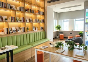Eine moderne Bibliothek mit Bücherregalen, einer grünen gepolsterten Bank und einem Tisch mit einem Buch und einer Tasse.