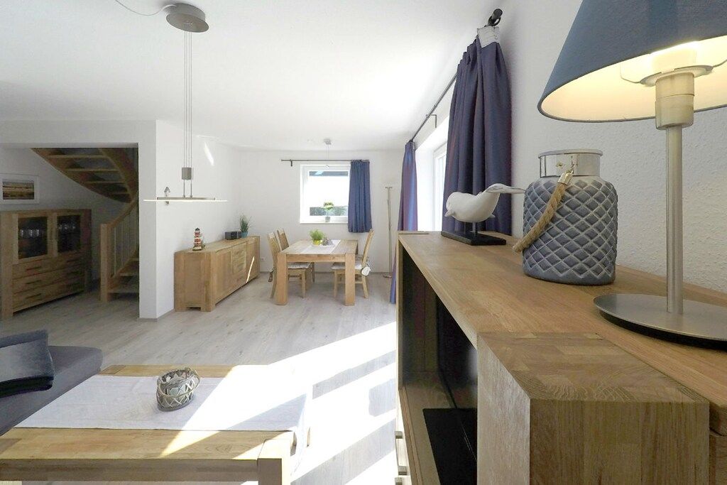 Et moderne opholdsrum med spiseplads, trappe og et stort vindue med gardiner.