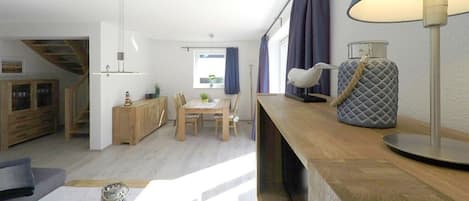 Et moderne opholdsrum med spiseplads, trappe og et stort vindue med gardiner.