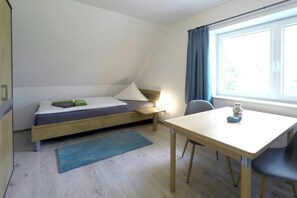 A compact room with a single bed, a small table, and a window with curtains. - Holiday home with 2 bedrooms (Dierhagen)