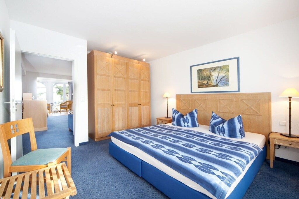 Quarto de hotel com uma cama grande, guarda-roupa de madeira, uma escrivaninha e uma cadeira.
