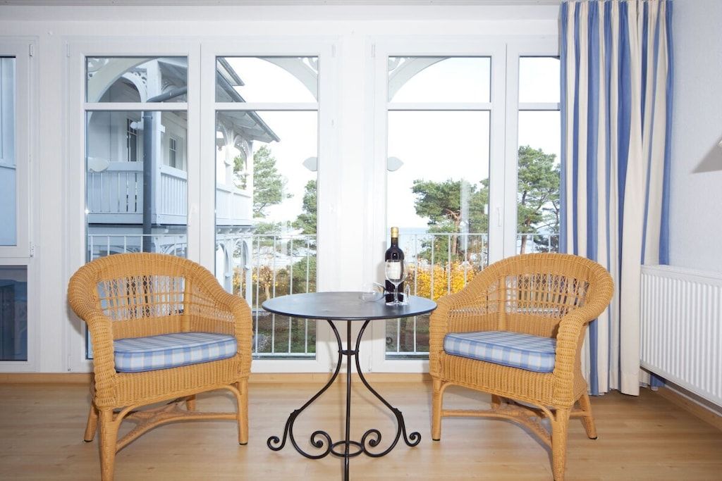 A room with two wicker chairs, a round table, and a view through large windows.