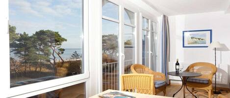 A balcony with a view of the sea, wicker furniture, and a table with a bottle and glasses.