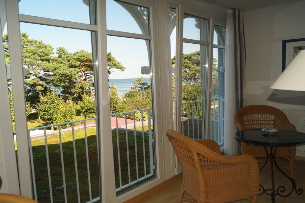 Un balcon avec vue sur la mer, des fauteuils en osier et une table.