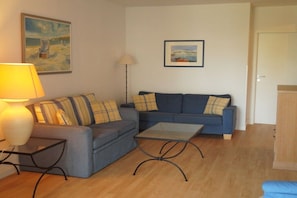A living room with a sofa, a coffee table, a lamp, and two paintings on the wall. - Villa Freia Apt. 20 Granitz (Ostseebad Binz)