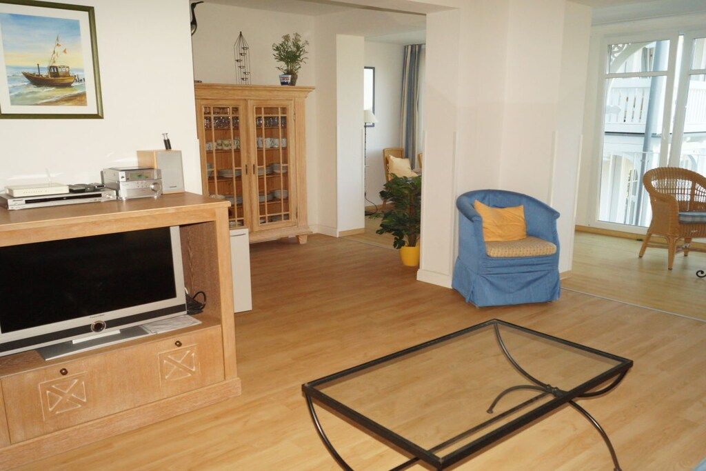 A living room with a television, wooden cabinet, blue armchair, and glass coffee table.