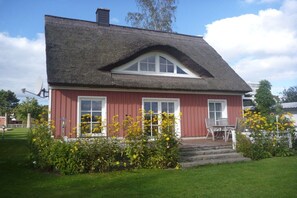 Ein rotes Haus mit einem Strohdach, weißen Fenstern und einer kleinen Veranda mit Stühlen.