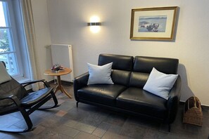 Ein modernes Wohnzimmer mit einem schwarzen Ledersofa, einem Schaukelstuhl, einem kleinen runden Tisch und einem gerahmten Bild an der Wand.