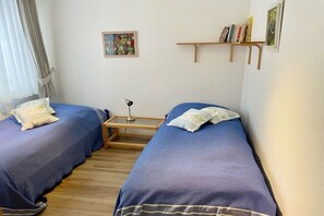 Ein Zimmer mit zwei Betten, einem kleinen Tisch, einem Bücherregal und einem Bild an der Wand.